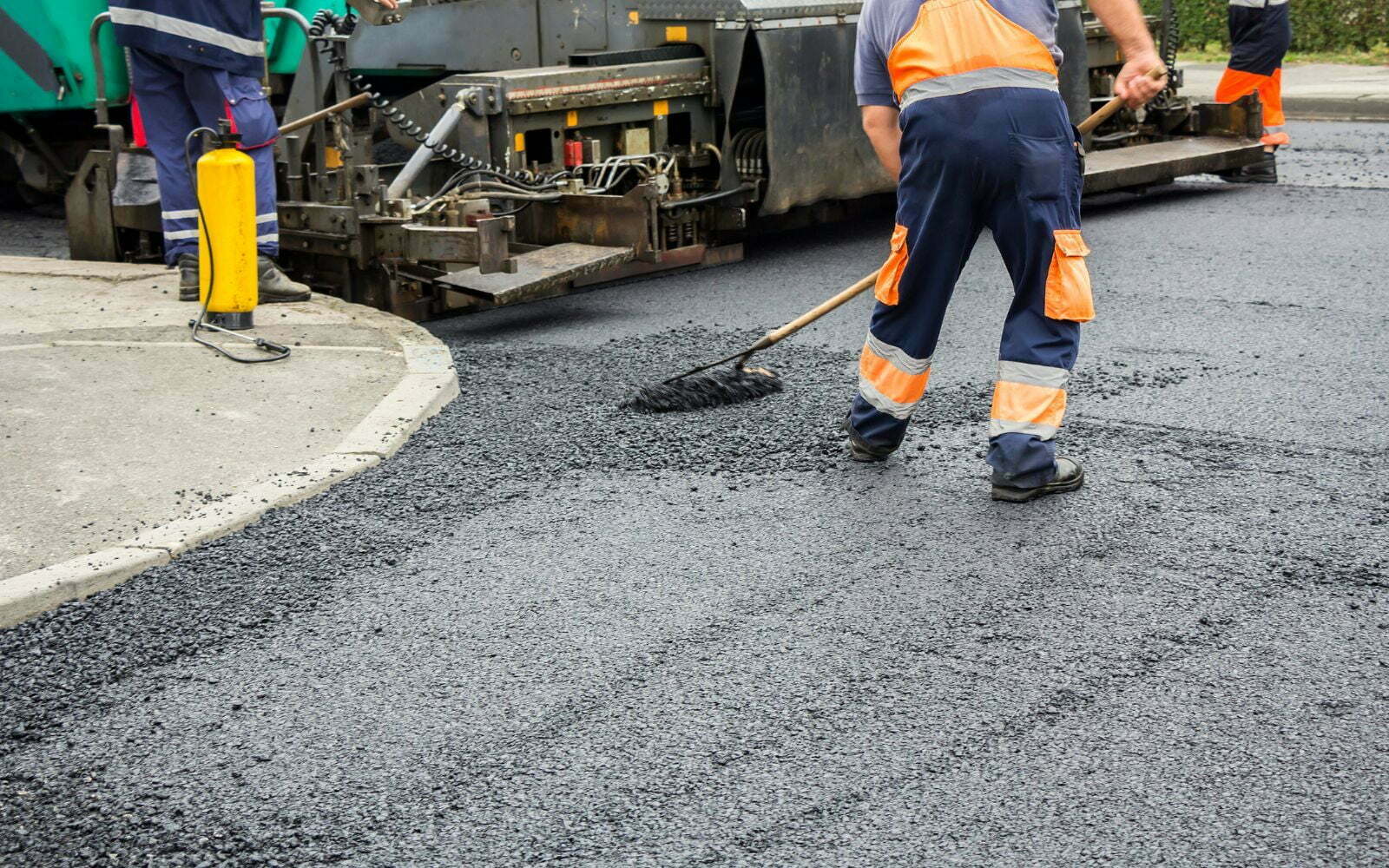 asphalt contractors Workers from a paving contractor in Annapolis, MD, using equipment to pave a road with asphalt, wearing safety gear and reflective clothing.