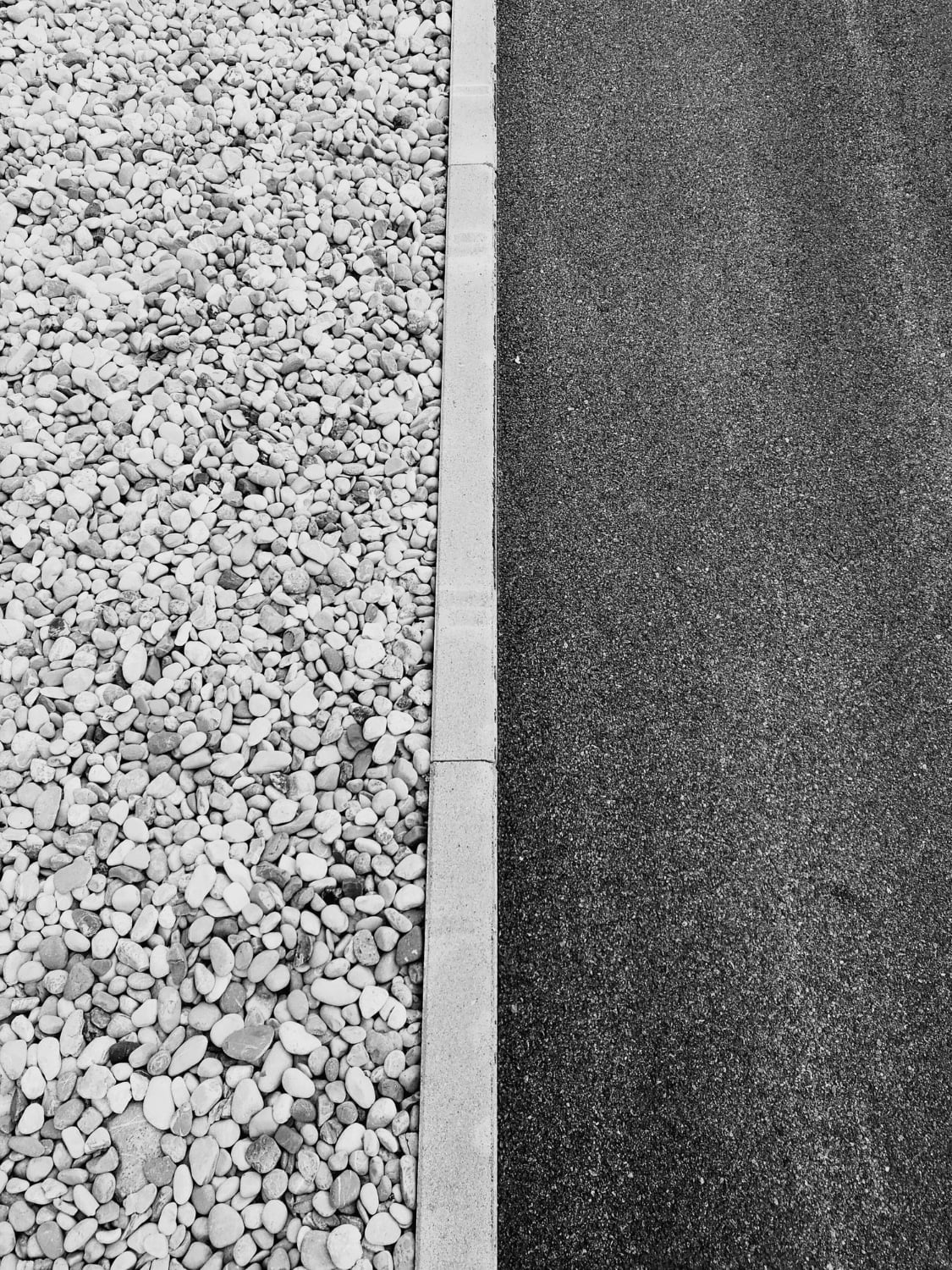 A black asphalt road in Maryland is bordered by a line of pebbles, separated by a straight concrete curb, crafted expertly by a paving contractor.