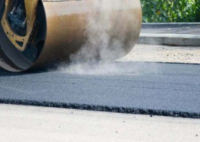 Steam roller smoothing fresh asphalt on a road, with visible steam rising.