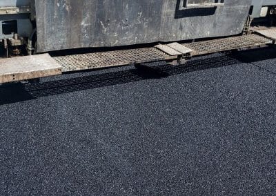 Machine laying fresh asphalt on a road, with a smooth, dark surface visible.