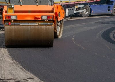 A road roller smoothing asphalt on a newly paved road, with a truck nearby.